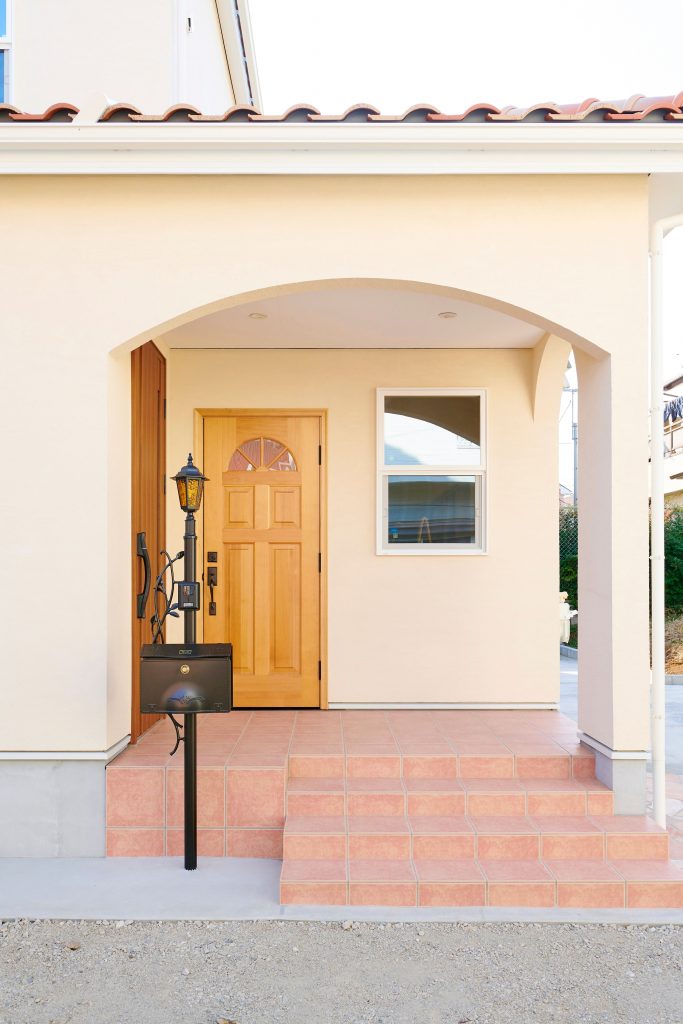 アーチの下がり壁にテラコッタ風タイルと木のドアで迎えてくれる温かみのある玄関。