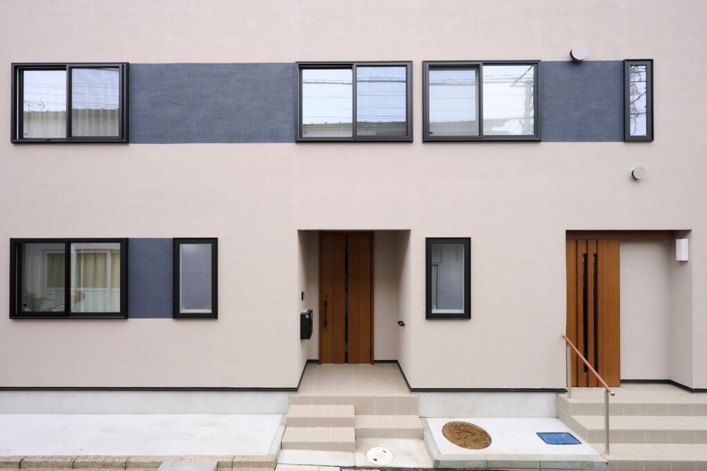 グレージュに濃いグレーの２トーンがリズムを奏でる外壁　左のドアは親世帯のお住まい、右の引戸は事務所のエントランス
